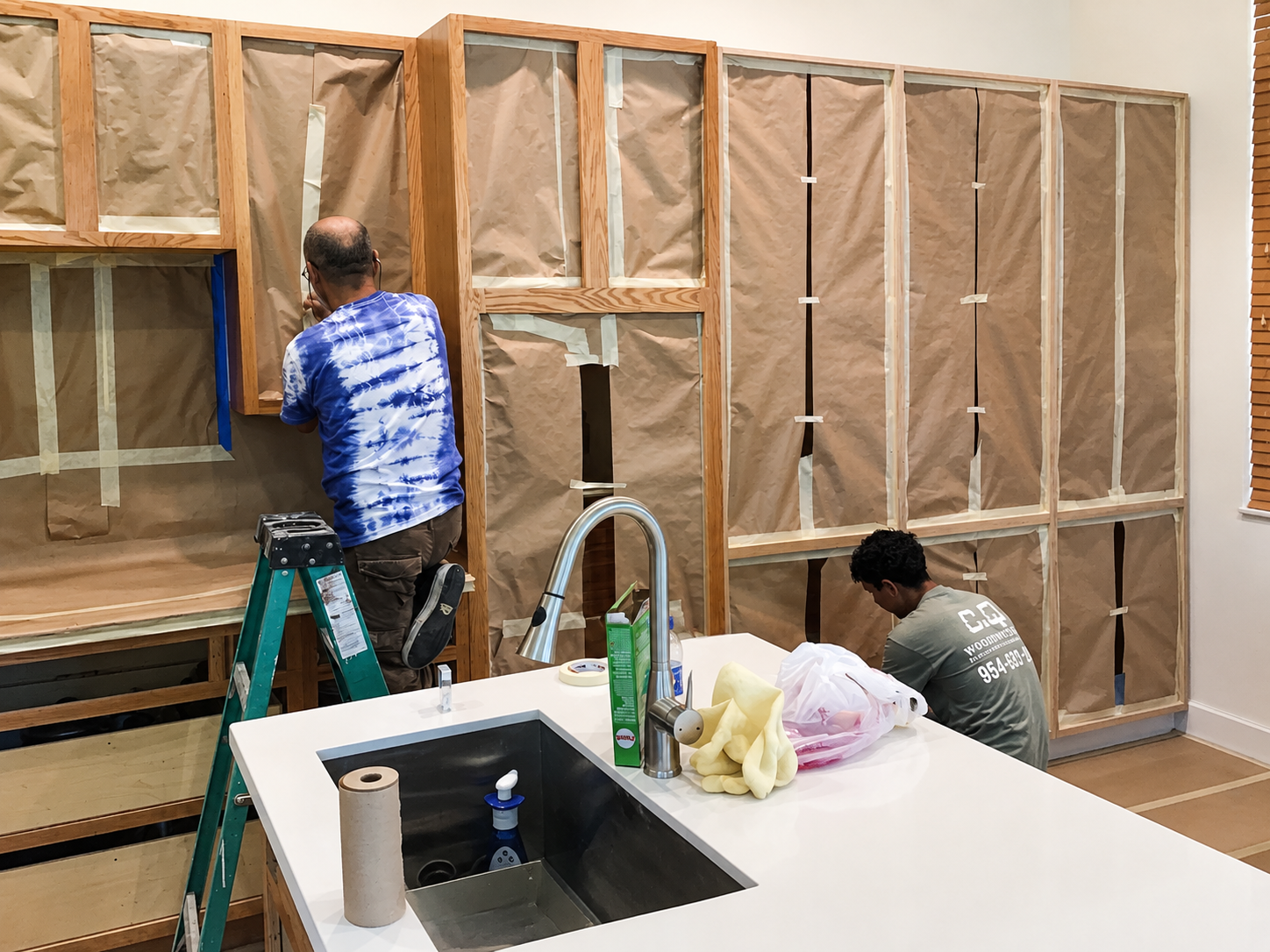 A full kitchen cabinet run fully masked with paper and tape ahead of refinishing