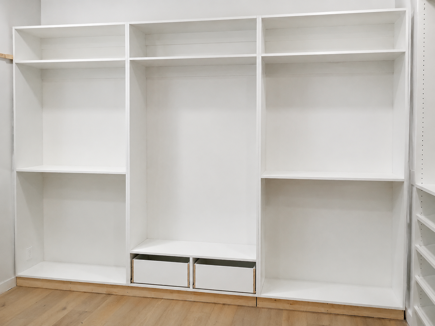 White three-bay closet built-in with open shelving and drawer boxes awaiting fronts