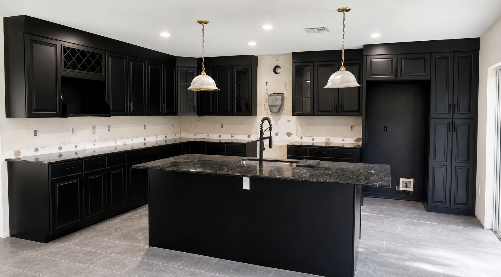 Black raised-panel kitchen with brass pendants, stone island, and full-height pantry cabinetry