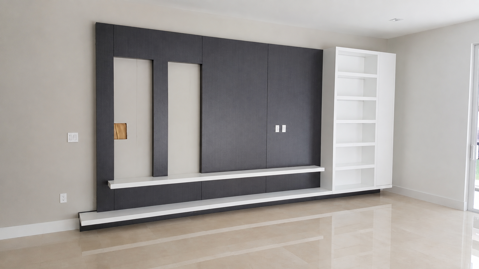 Floor-to-ceiling media wall in dark charcoal panels with white floating shelves