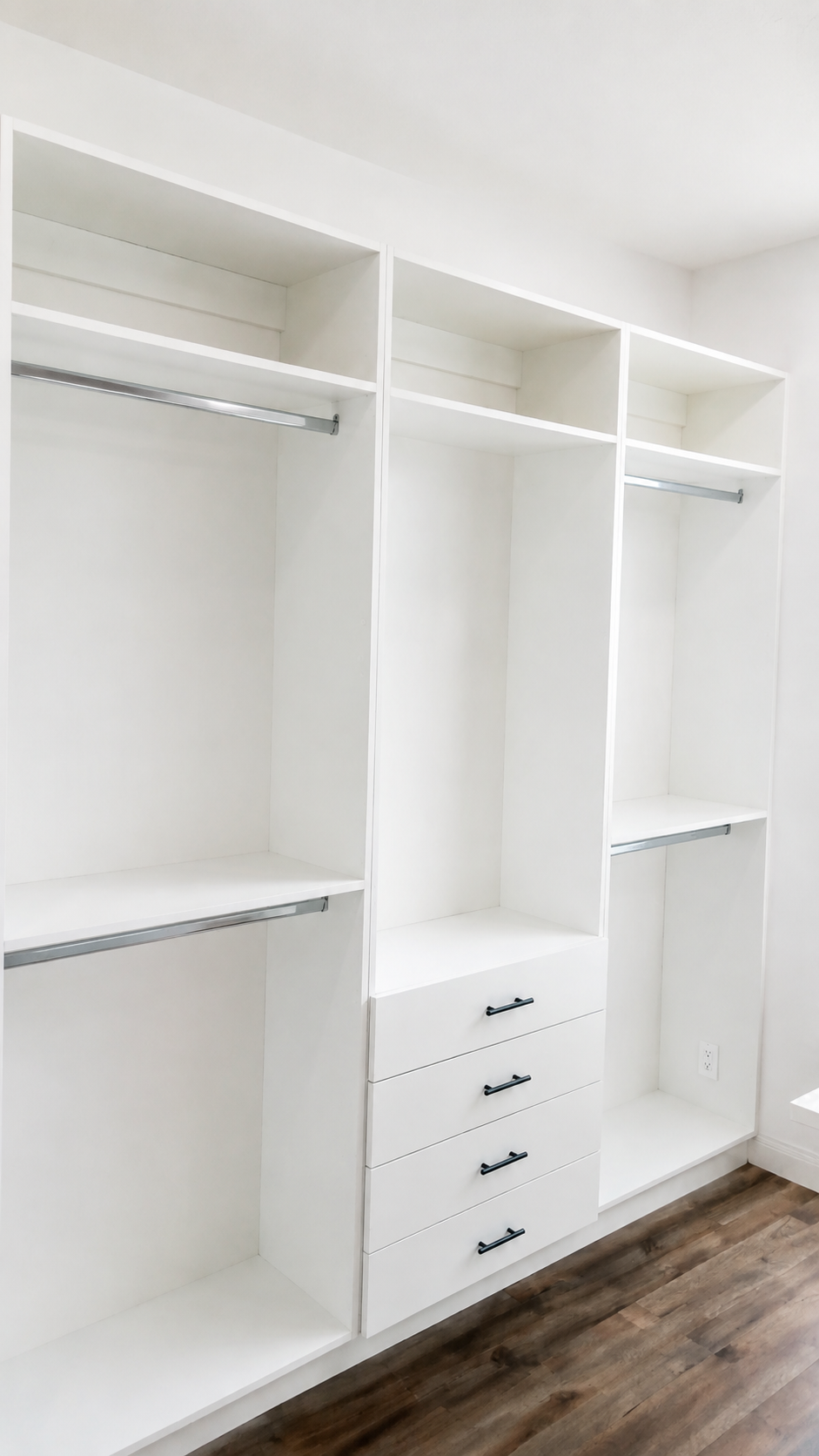 White closet built-in with chrome hanging rods, shelving, and center drawers