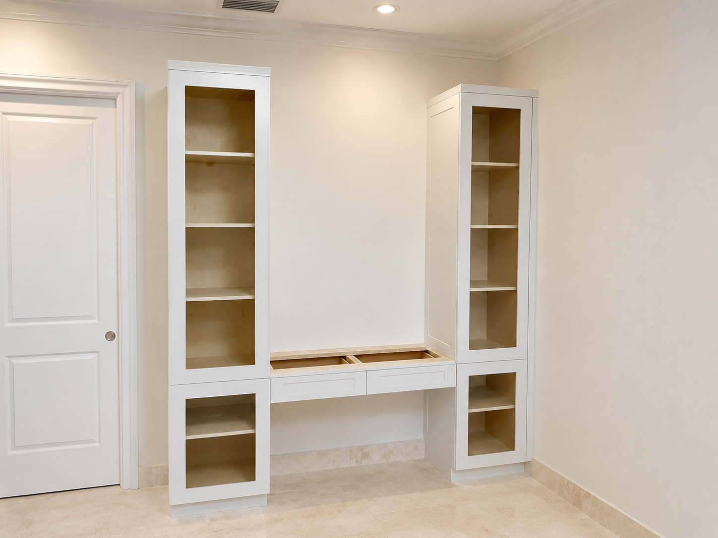 Paired white built-in bookcases with glass doors flanking a desk