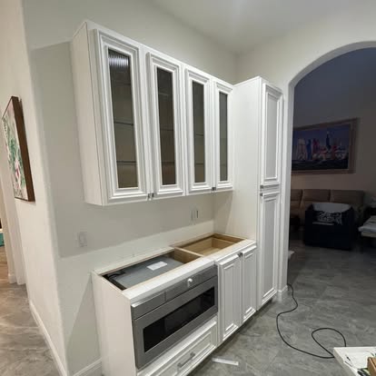 Painted cabinetry with glass-front upper doors partway through installation