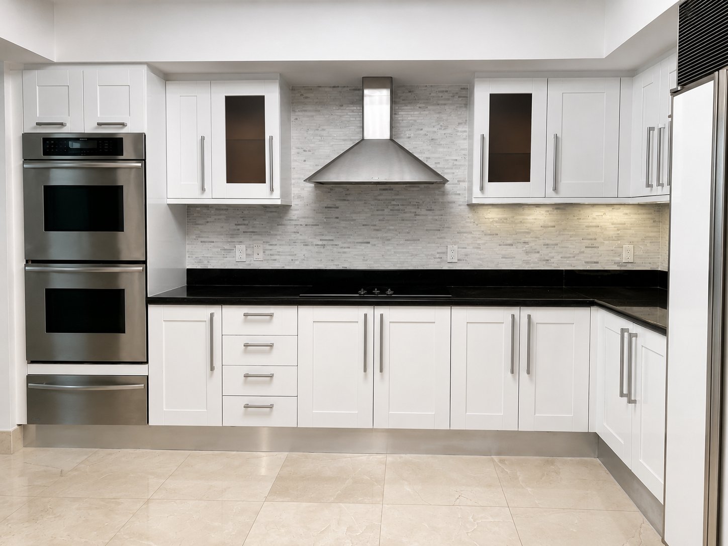 White Shaker kitchen with glass-front upper doors, black countertops, and stainless appliances