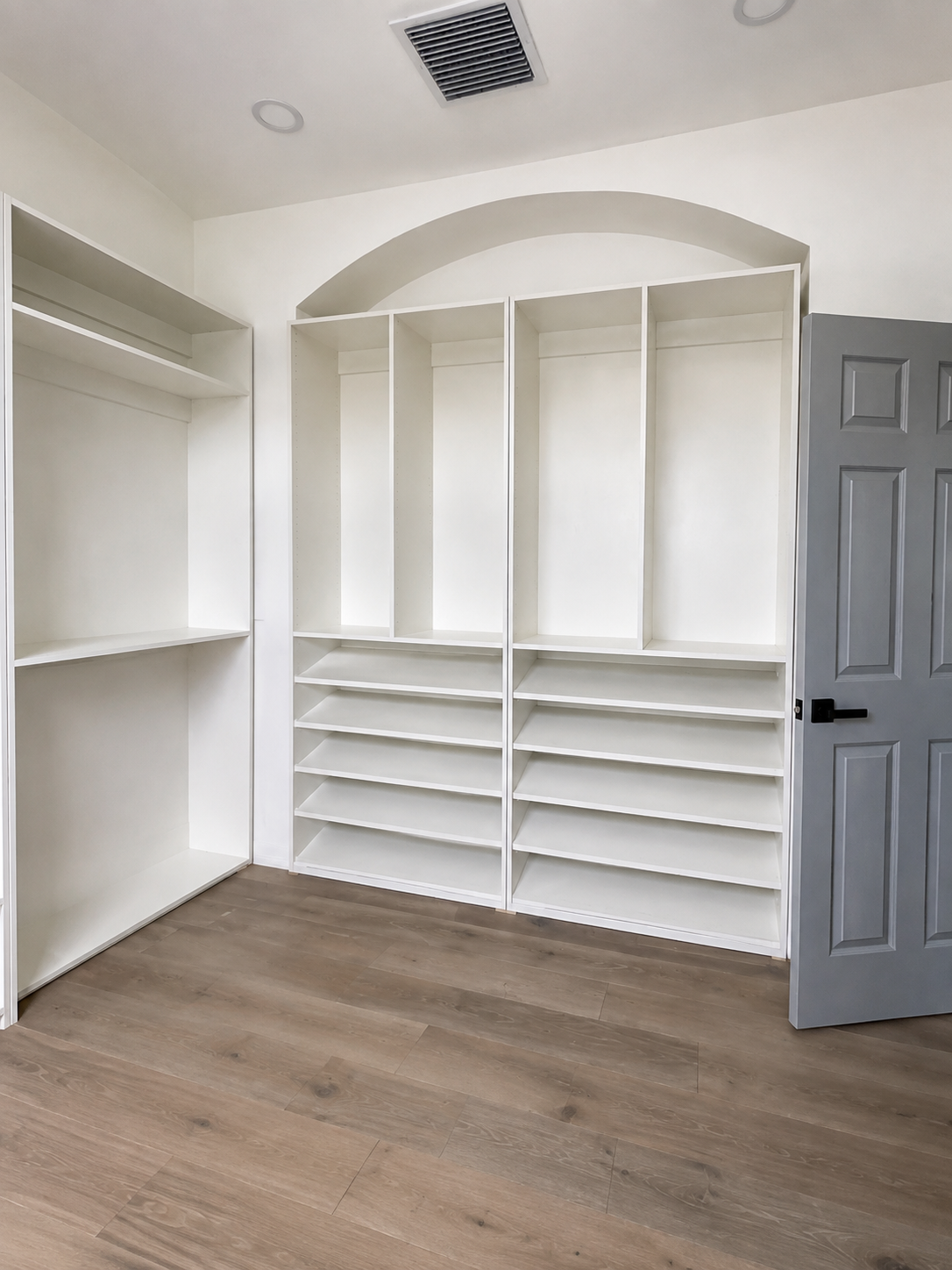 White closet built-in with arched top, upper hanging sections, and shoe shelving